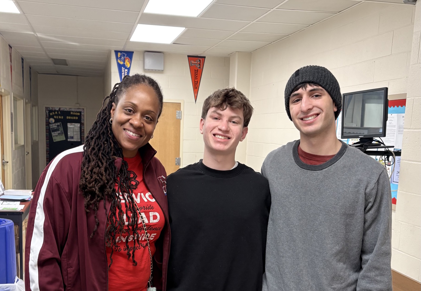 Mrs. Anikya, Principal of James G. Blaine Elementary & Middle School, with the Teach It Forward founders in a hallway lined with college pennants